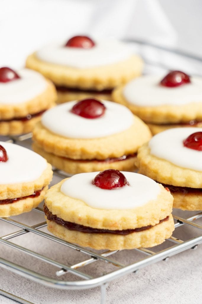 Scottish Empire Biscuits on a cooling rack - Shortbread with jam, icing, and a cherry on top