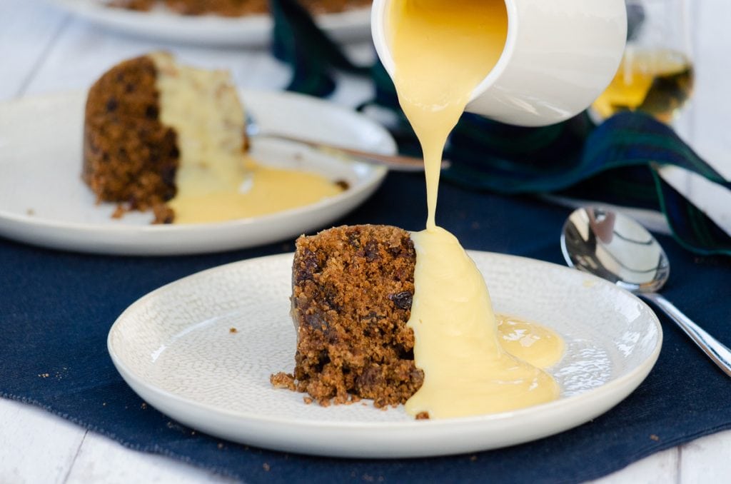 Clootie Dumpling on a plate with a jug of custard being poured over it